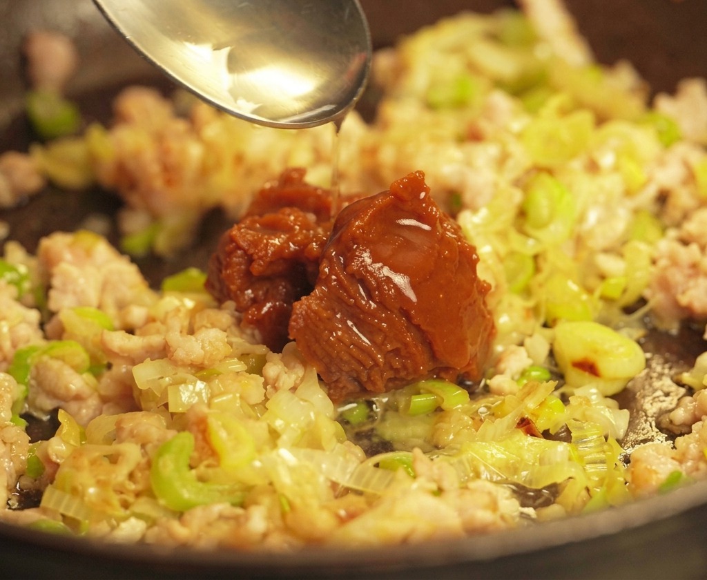 炒めた豚肉とねぎの上に、スプーンで味噌を加えている様子