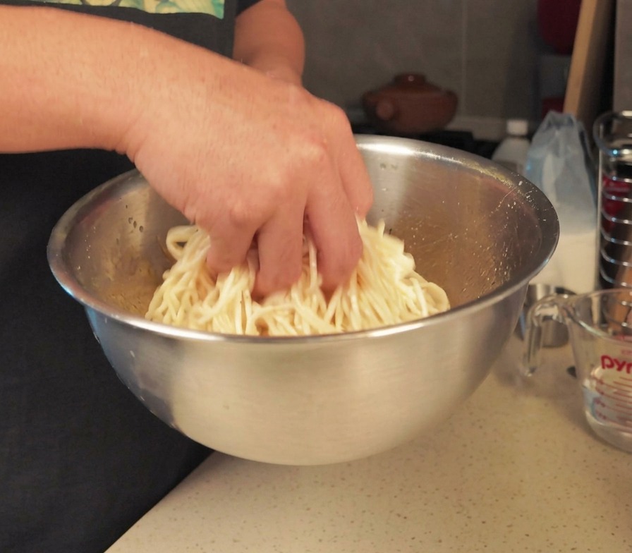 ボウルに入った茹でたての麺にごま油を絡めている様子