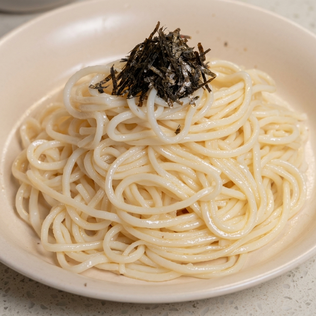 器に盛られた白い麺の上に、細切りにした黒い海苔をふんわりと乗せている様子