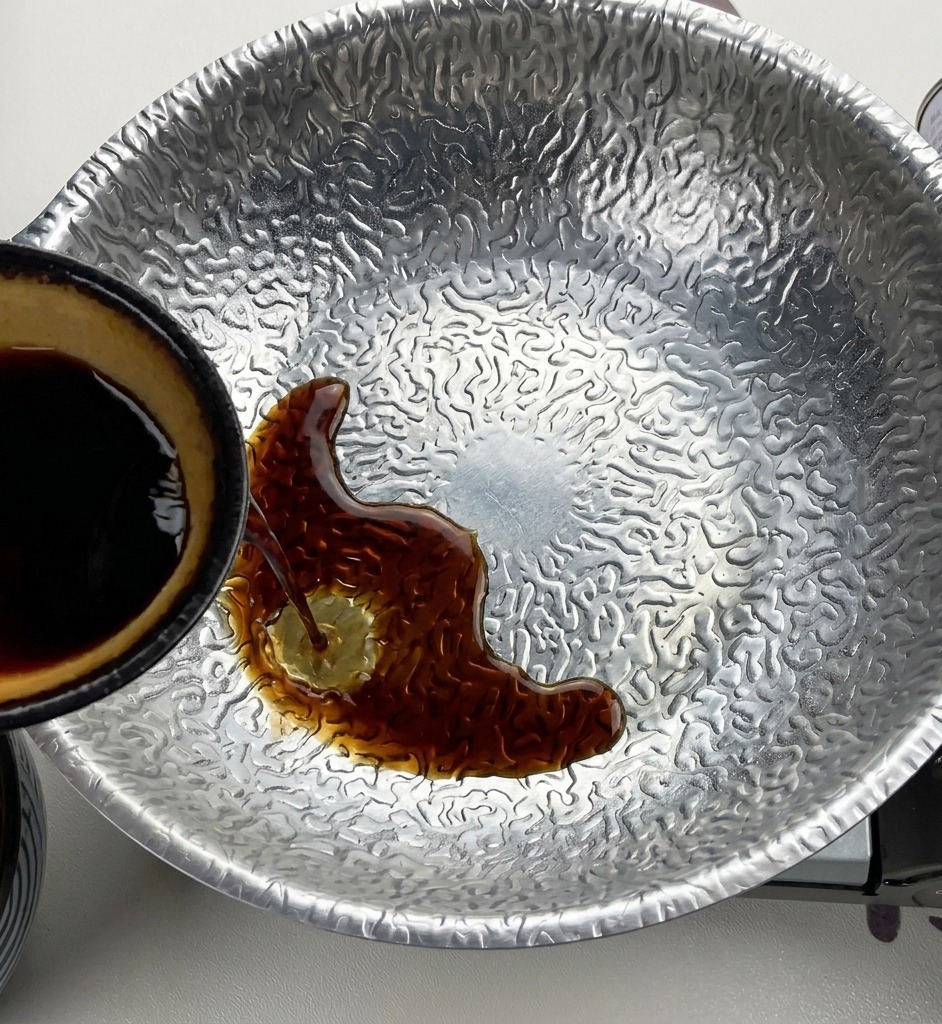 内側が黄色の小鉢から、味噌と砂糖の入った鍋に濃口醤油を注ぎ入れている様子。
