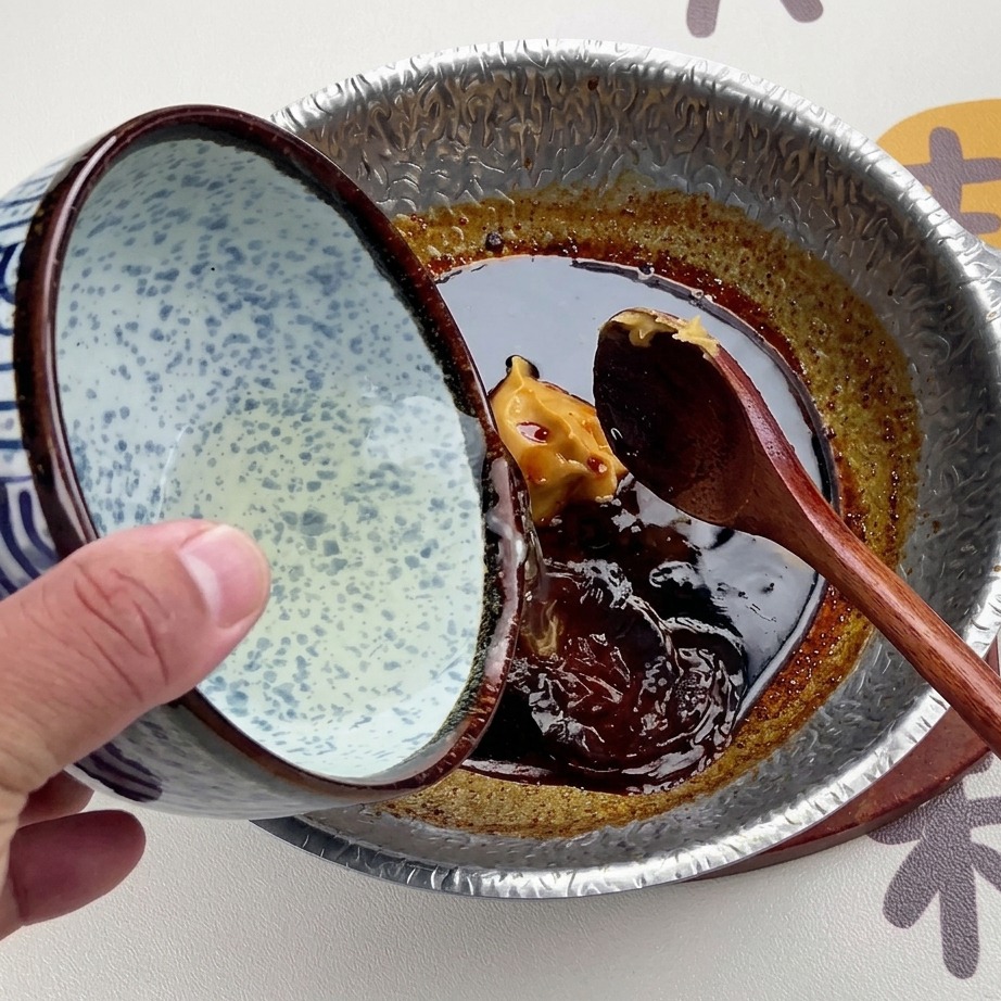青と白の模様の入った陶器の器から、濃い味噌だれに出汁を注いでいる様子。