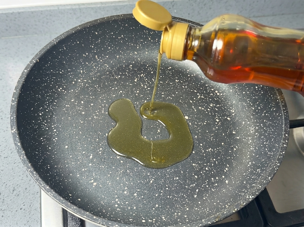 黒い斑点模様のある焦げ付き防止フライパンに、ボトルからサラダ油を注いでいる様子。