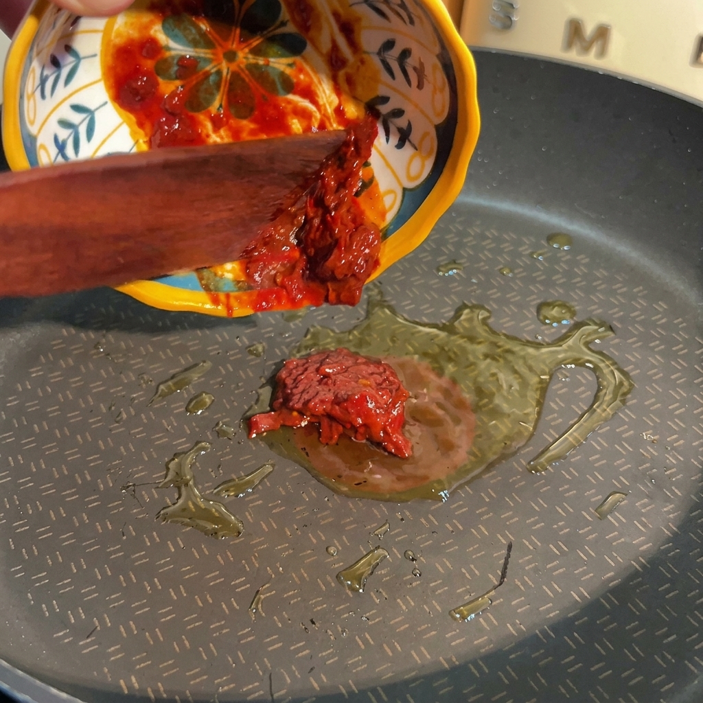 木製ヘラを使い、お皿から熱した油の入ったフライパンへと赤い豆板醤を入れる様子。