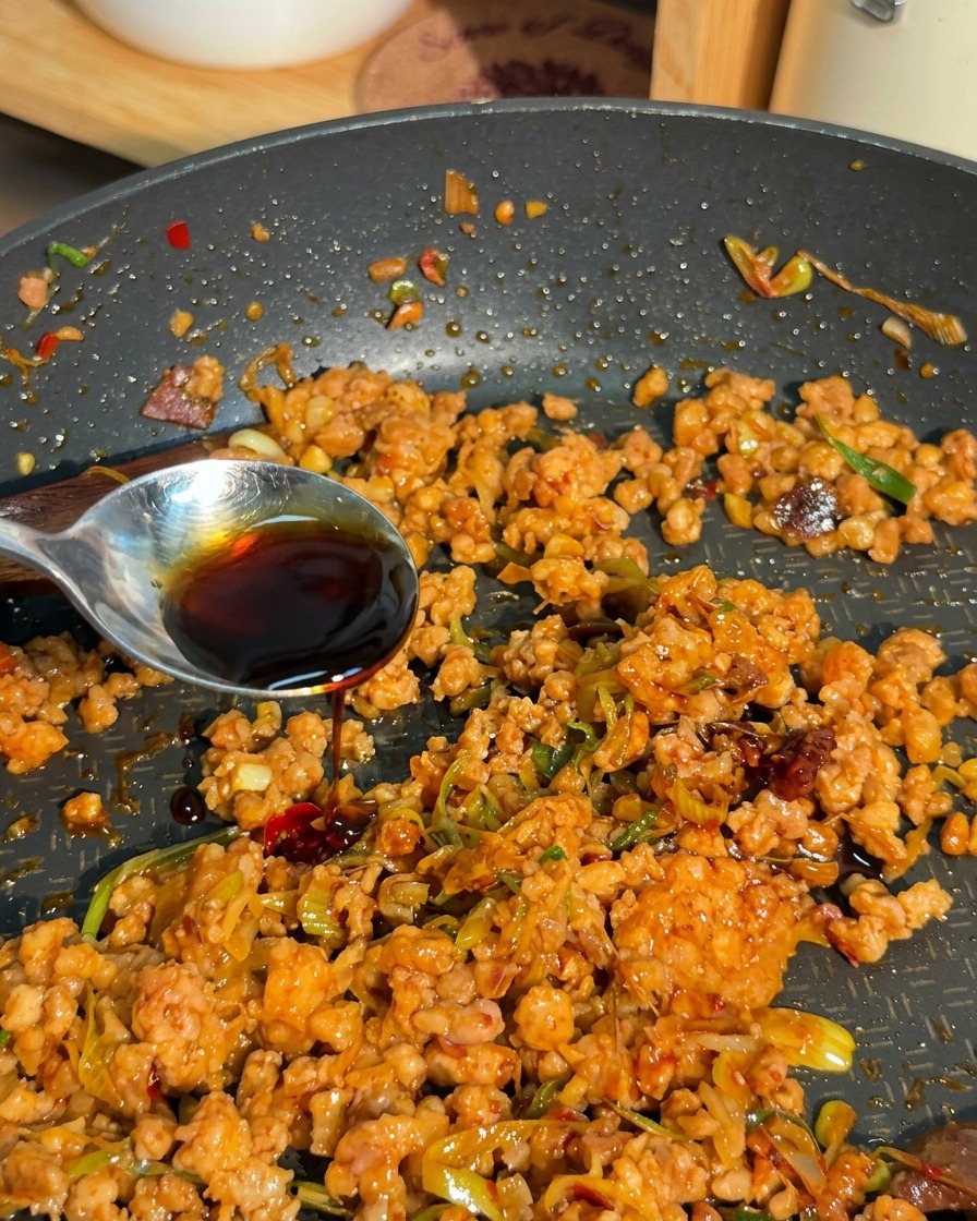 炒めたひき肉のフライパンに、スプーンを伝わせながら濃厚な液体を注ぎ入れている様子。