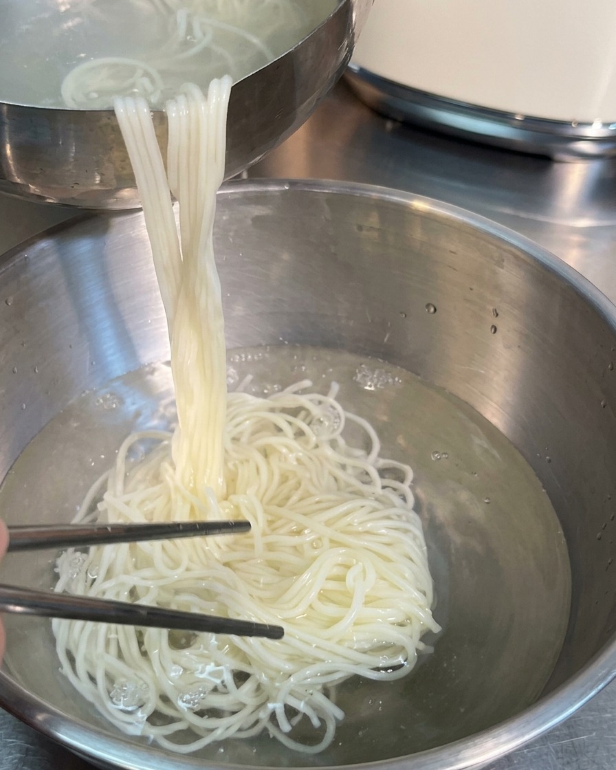 ステンレスの箸を使い、茹で上がった麺を冷水の入ったボウルへと移している様子。