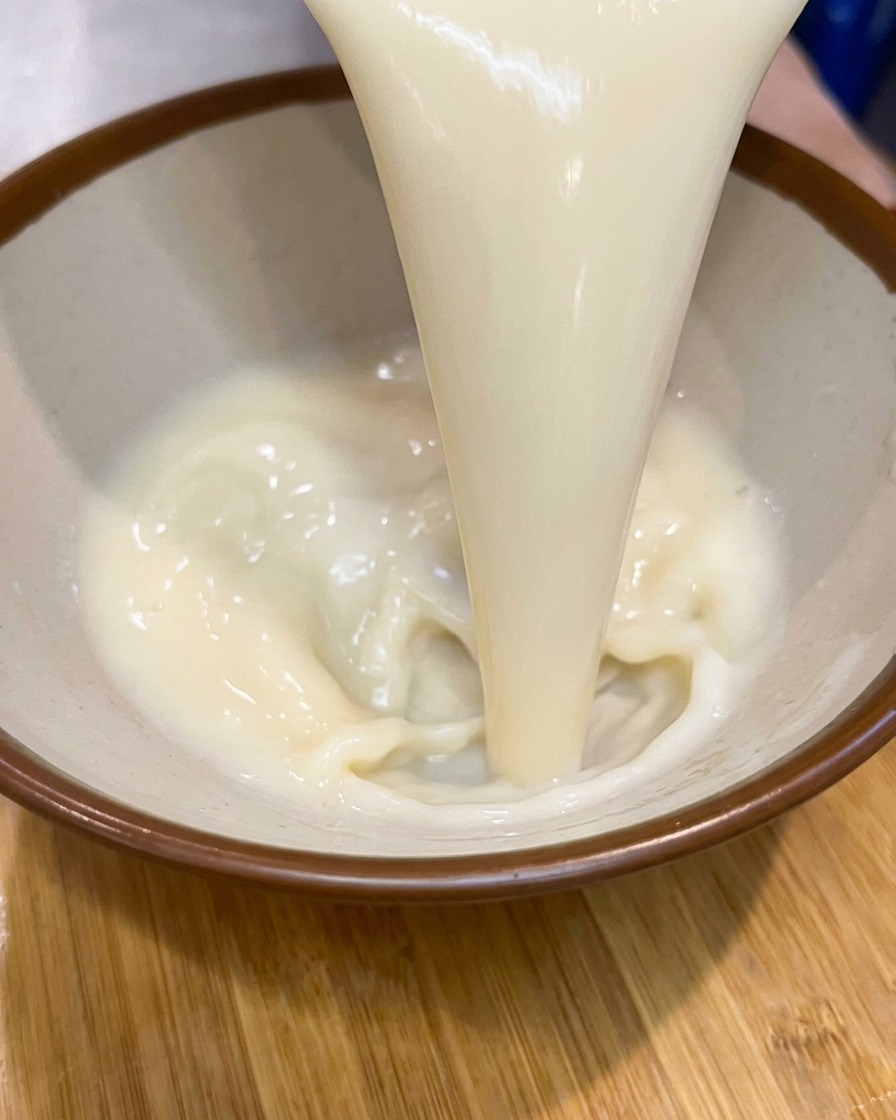 茶色の縁取りがある陶器のラーメン鉢に、白濁したクリーミーなスープベースが注がれている様子
