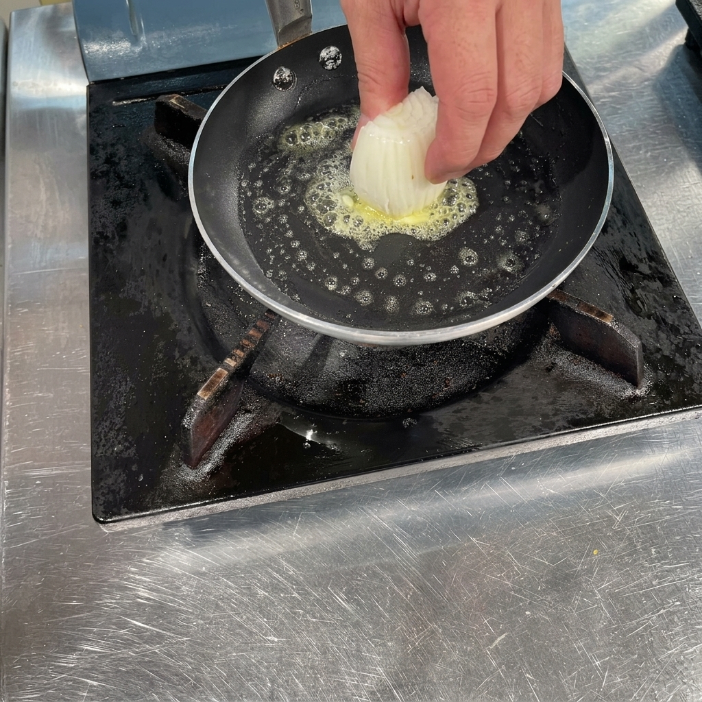 泡立つ溶けたバターが入った熱いフライパンに、スライスした玉ねぎを投入する様子