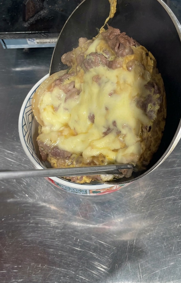白米の入った丼ぶりの上にフライパンを傾け、牛肉ととろけるチーズが一体となって滑り落ちるようにのる様子