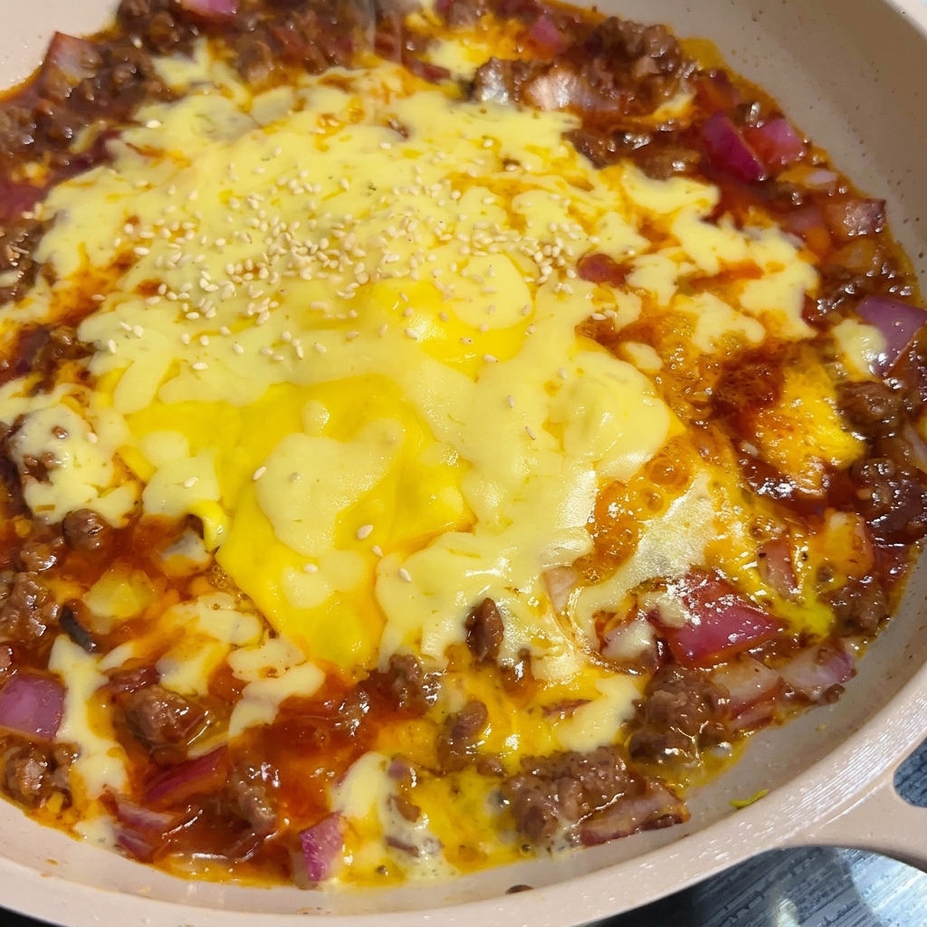 牛肉と玉ねぎの上で白と黄色のチーズがとろりと溶け、仕上げに白ごまが軽く振られた料理のクローズアップ。