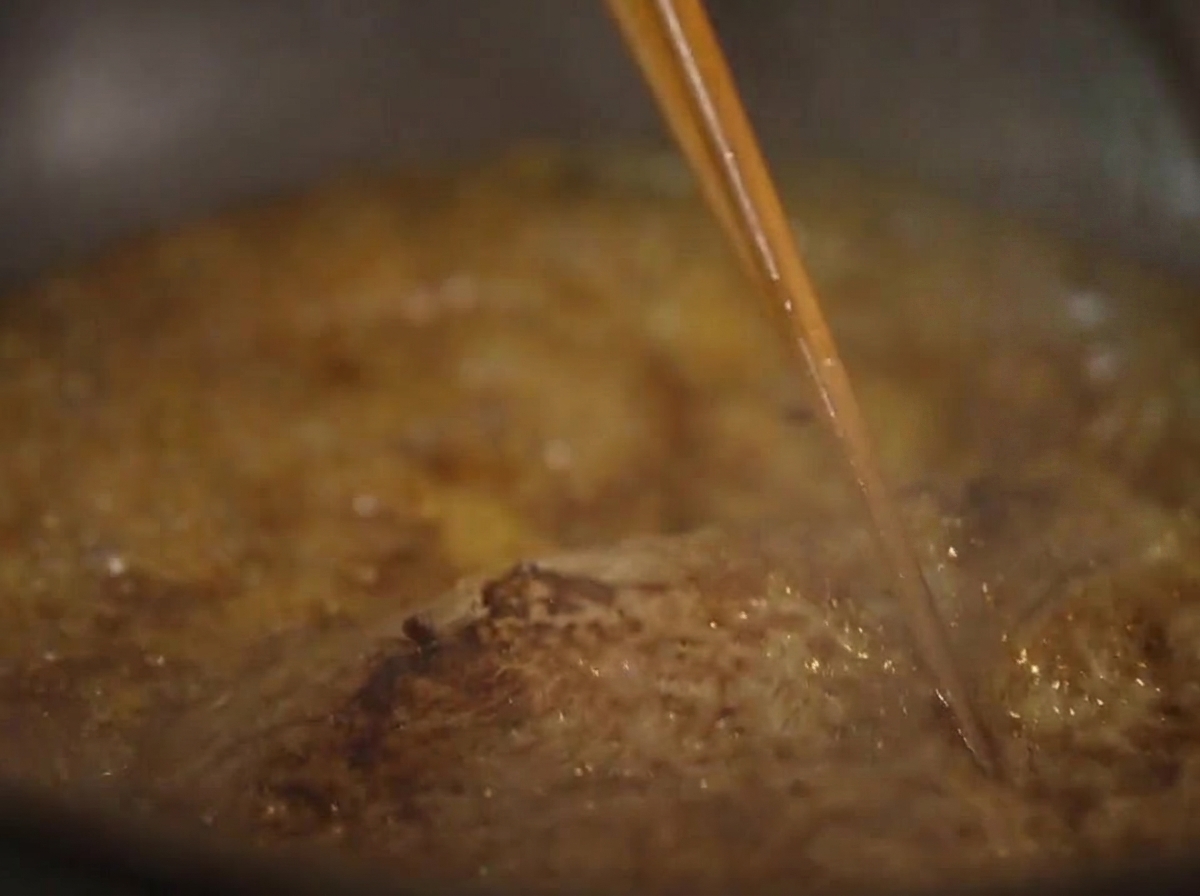 濃厚に泡立つ茶色いソースの中で煮込まれているステーキに、箸を使って何度もソースを絡めているクローズアップ写真。
