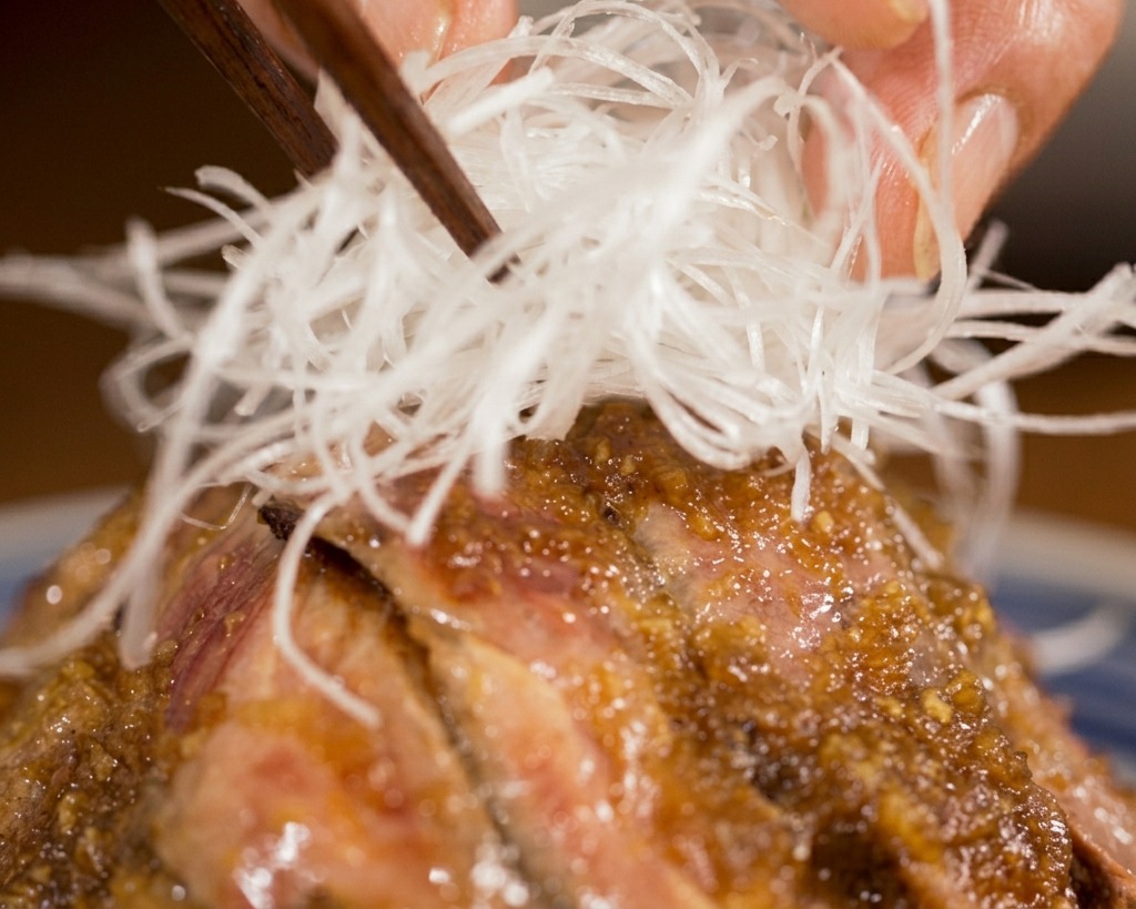 箸を使って、ソースがかかったステーキ丼のちょうど中心に、細く切った白髪ねぎをこんもりと盛り付けている様子。