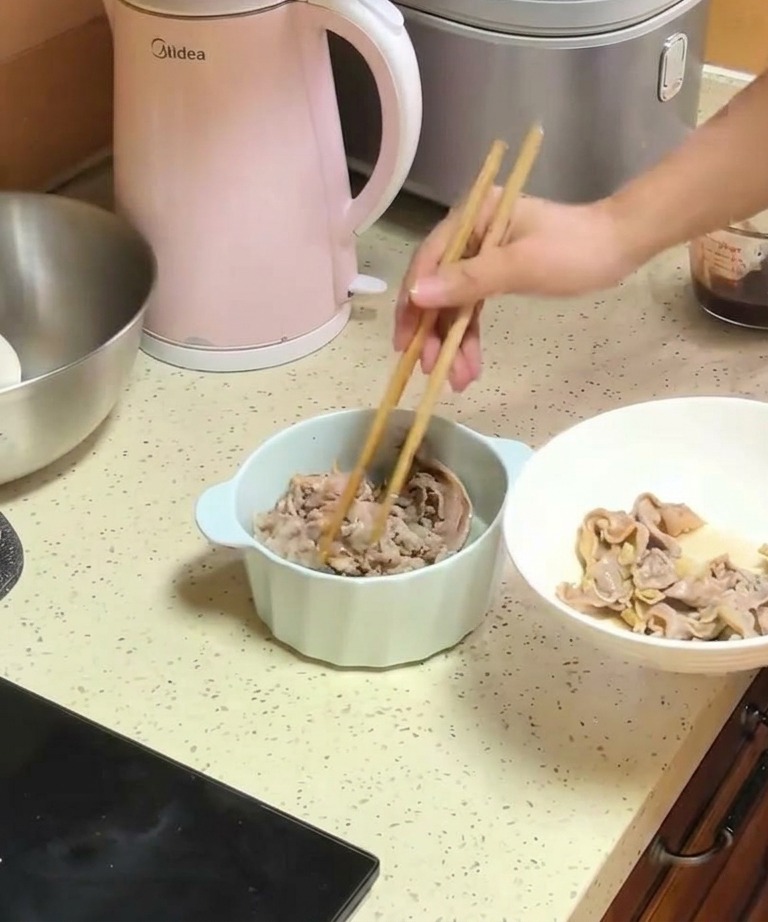 加熱した玉ねぎが入ったボウルに、木箸を使って白いお皿から湯通しした牛肉を移し替えている様子。