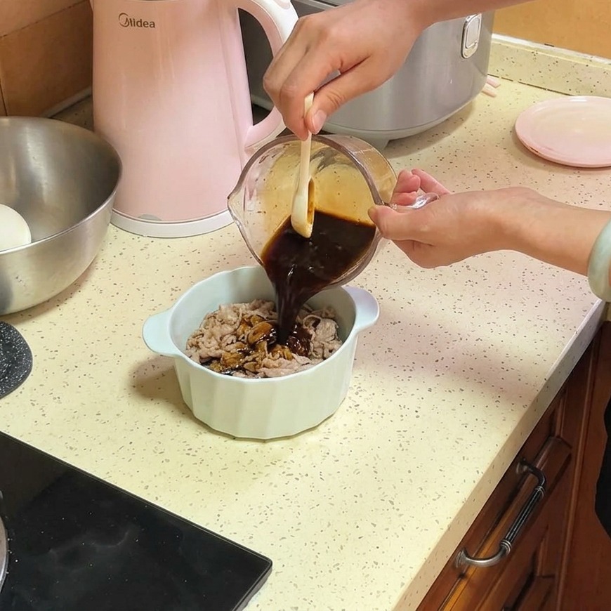 白いセラミックボウルに入った牛バラ肉と玉ねぎの上に、ガラスの計量カップから濃い茶色の特製ダレを注いでいる様子。