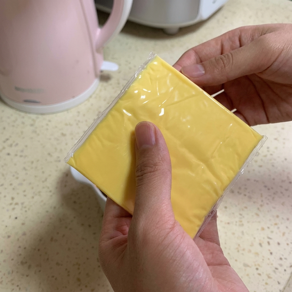 牛肉と濃いタレが入ったボウルの上に、四角い黄色いスライスチーズを2枚重ねて乗せようとしている様子。