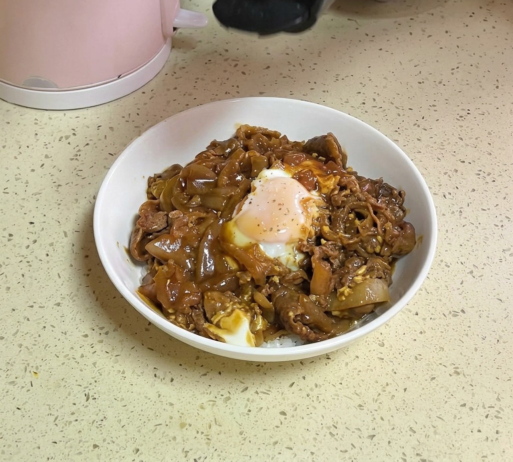 出来上がったチーズ牛丼の上に、容器から白ごまとドライパセリを振りかけている様子。