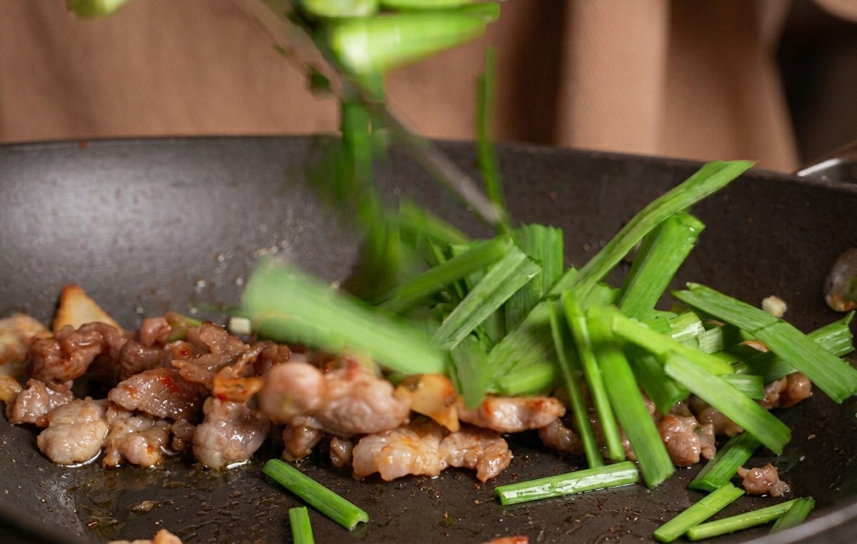 牛肉とキムチが炒められているフライパンの中に、手元から刻んだ緑の小ねぎが投入される瞬間。