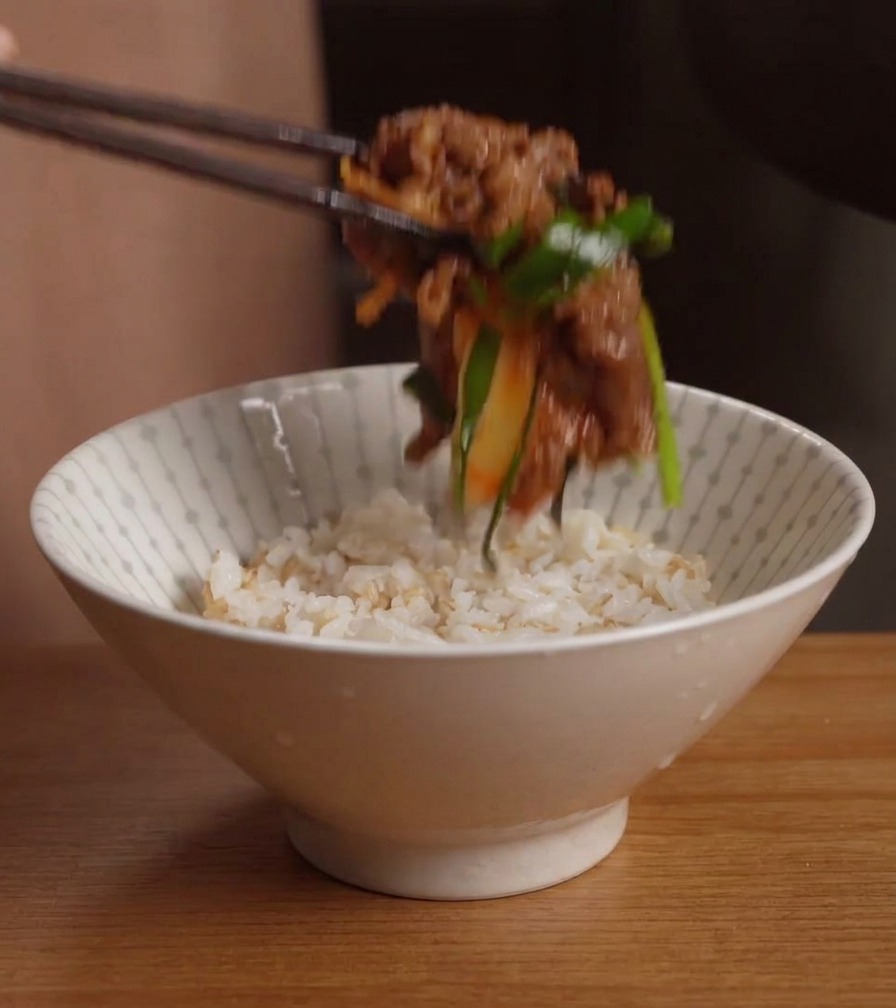 ほかほかのご飯が盛られた白い丼に、お箸を使って炒め立てのキムチ牛カルビをたっぷりとのせている様子。