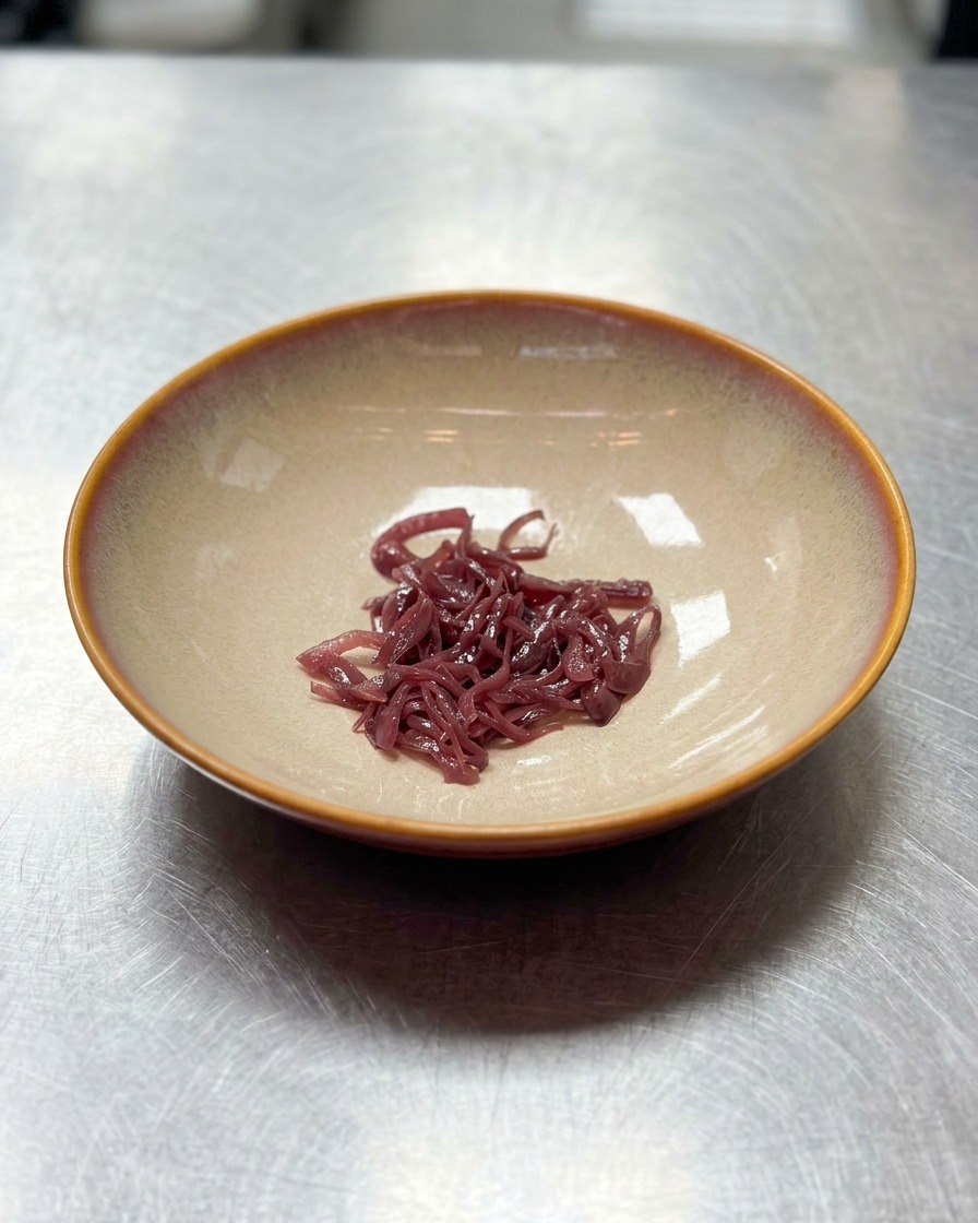 大きめで平らなベージュのセラミック製の丼の中央に、少量の千切りにした紫玉ねぎが盛られている様子。