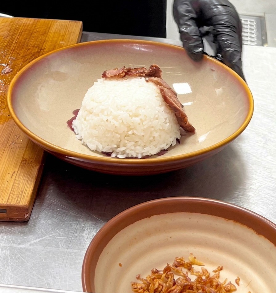 手袋を着用した手が、ドーム状に盛られたご飯の周りにスライスした牛肉を丁寧に並べ、火山のような形を作っている様子。