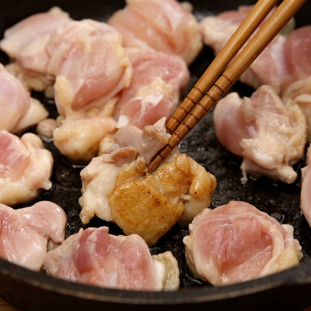 お箸を使い、フライパンの中でほんのり焼き色がつくまで鶏もも肉を炒めている様子。