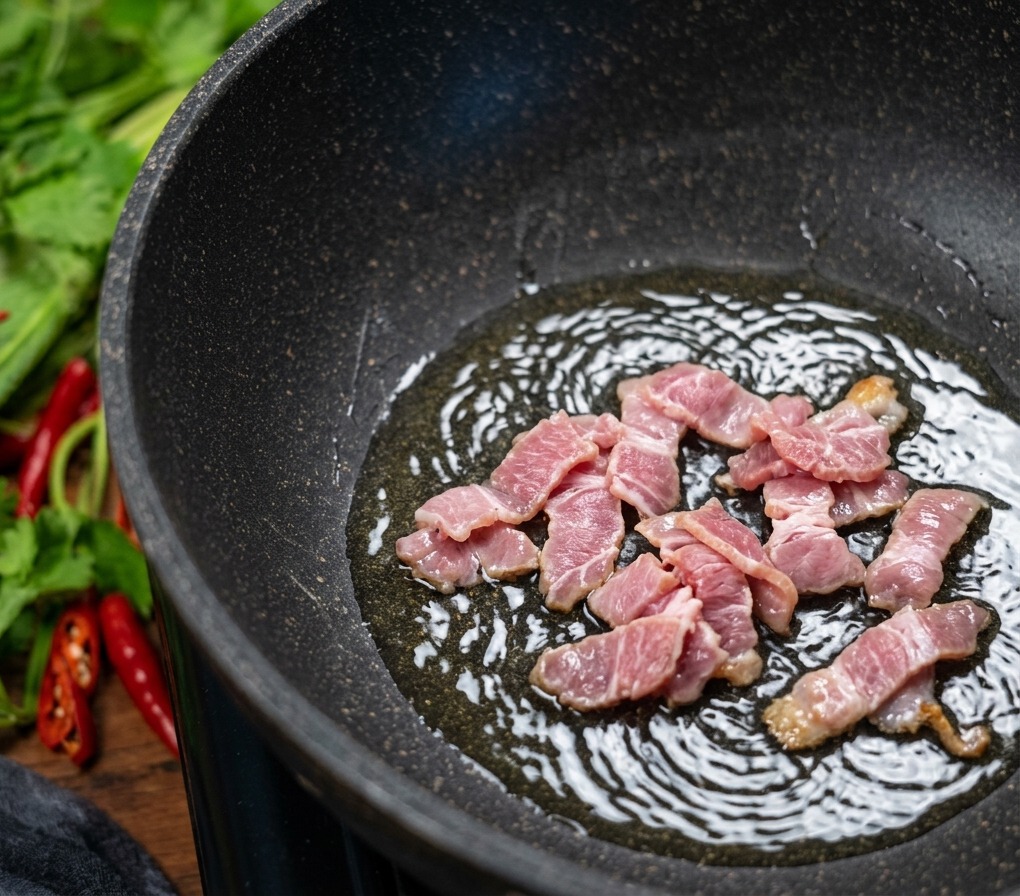 フライパンの中で油を出しながら香ばしく色づくまで炒められているベーコン