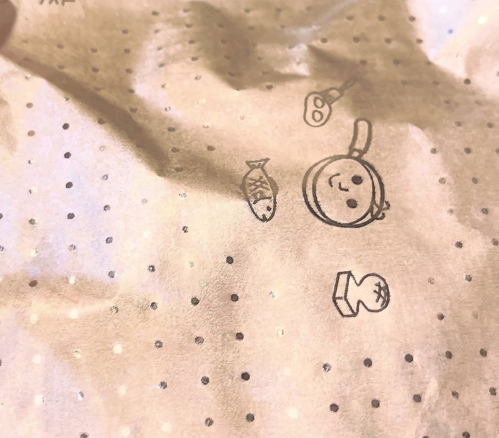 調理中のフライパンの上に、キッチンのイラストが描かれた円形のクッキングペーパー製の落とし蓋が被せられている接写カット。