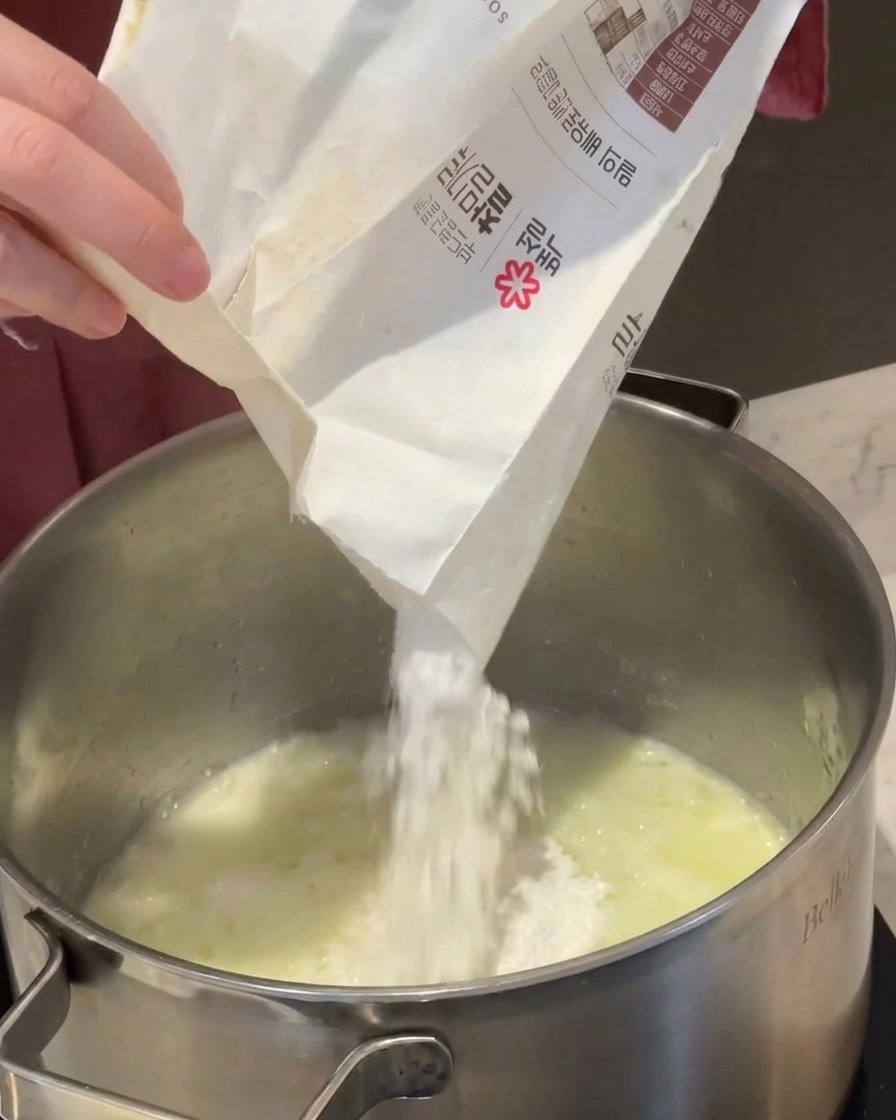 溶けたバターと玉ねぎが入った鍋に、薄力粉を加えている様子