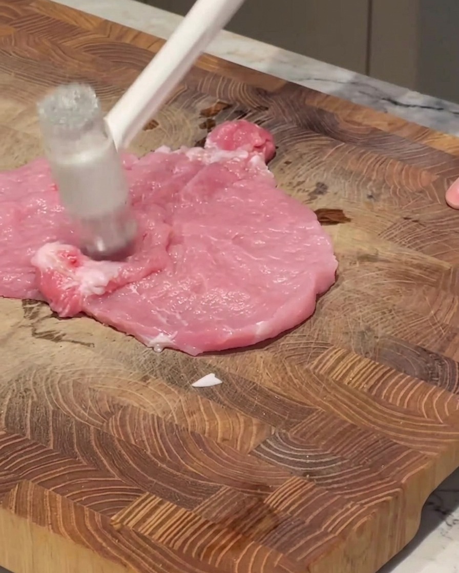 まな板の上で、肉叩きを使って生の豚ロース肉を叩いている様子