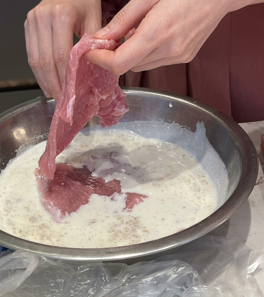 にんにく入りの白いミルクマリネ液に、生の豚肉を浸している様子