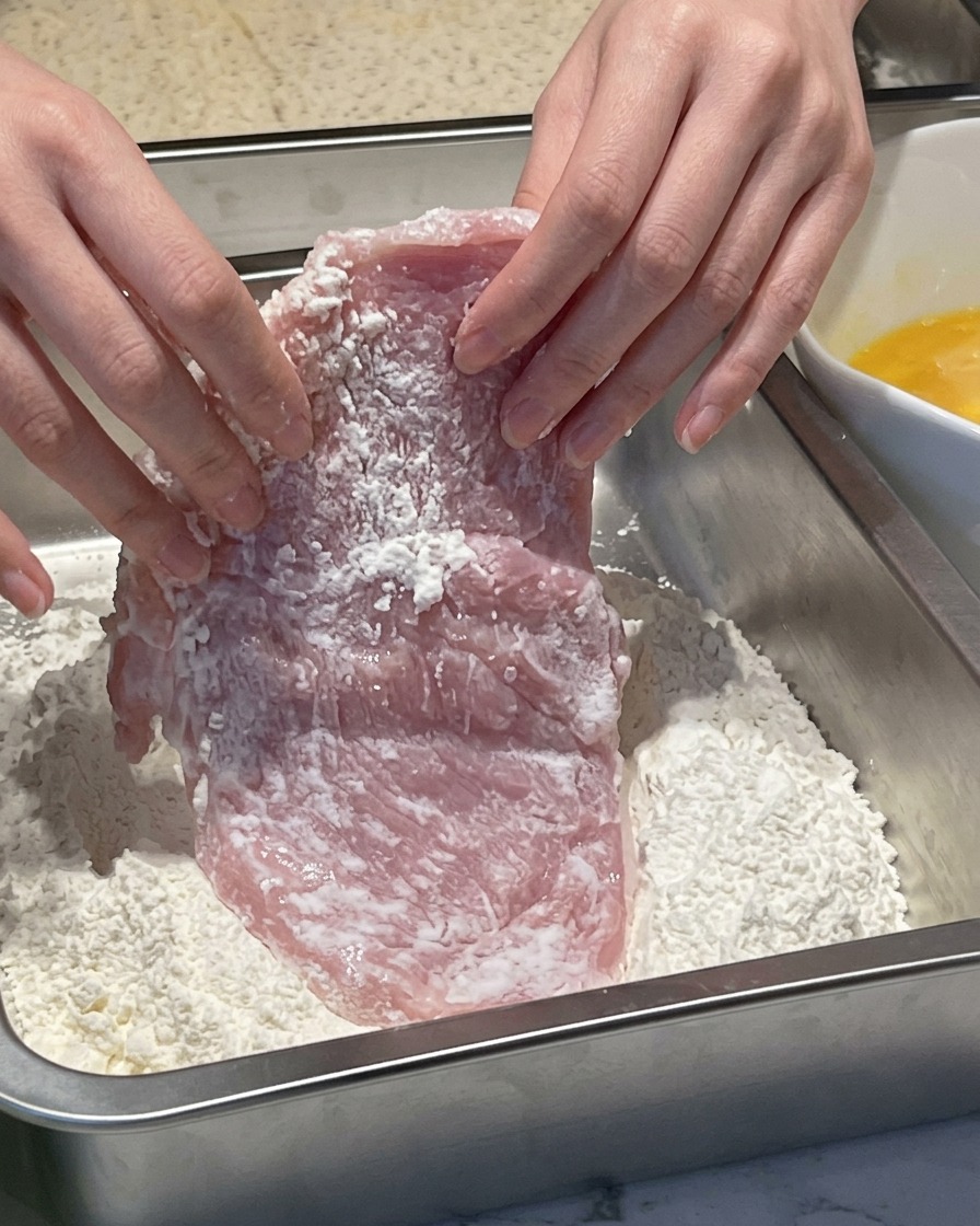 薄力粉が入ったバットに、お肉を押し当てて粉をまぶしている様子