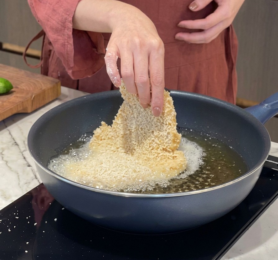 熱した揚げ油の中に、衣をつけた豚カツを静かに入れている手元の様子