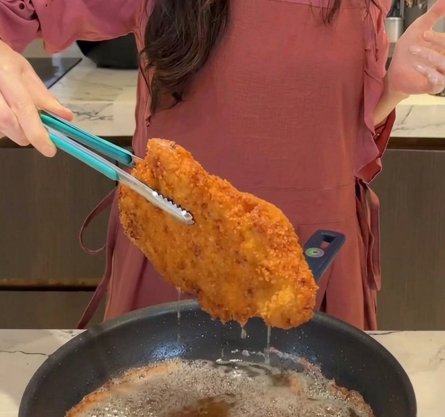トングを使って、揚がったサクサクのとんかつを鍋から引き上げ、油を切っている様子
