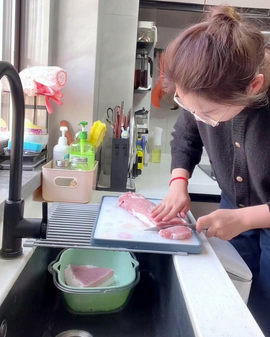 白いまな板の上で、キッチンナイフを使って生の豚ロース肉を厚さ約1cmのサイズに均一に切り分けている様子。