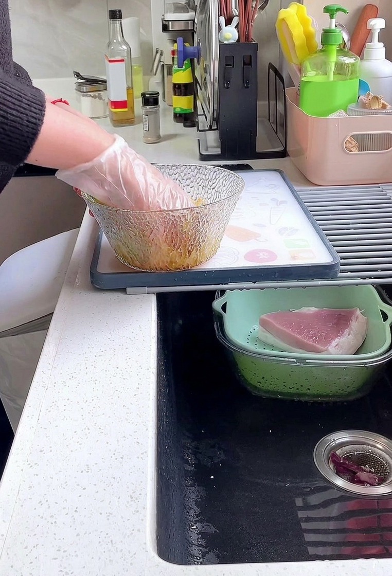 ビニール手袋を着用した手が、ガラスボウルの中で豚ロース肉としょうゆ、こしょう、片栗粉をしっかりと揉み込んでいる様子。