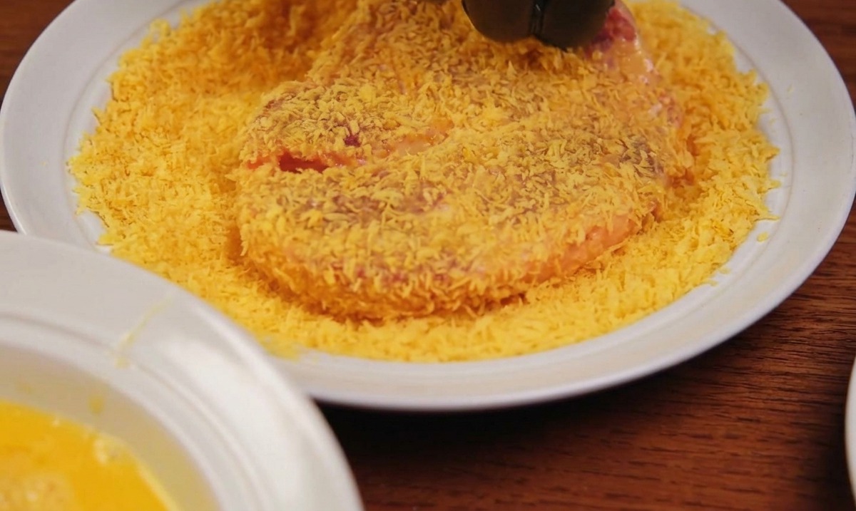 パン粉が敷き詰められたバットの中で、豚肉を上からしっかりと手で押さえている様子。