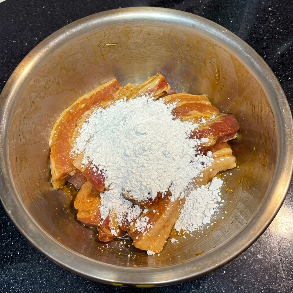 ボウルに入った濃い茶色の味付け豚肉の上に、白い粉末状のさつまいも粉がこんもりと盛られている様子。
