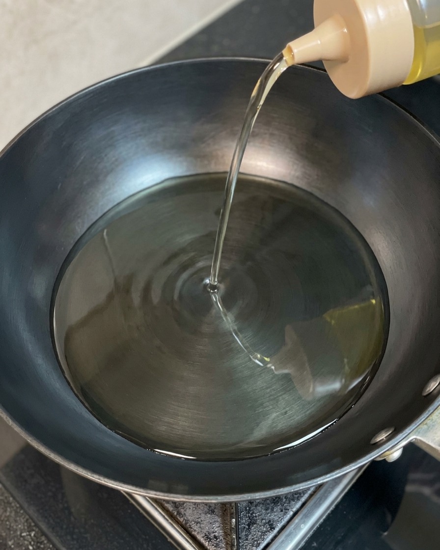 スクイーズボトルから、熱せられた黒い中華鍋に澄んだ揚げ油が注がれている様子。