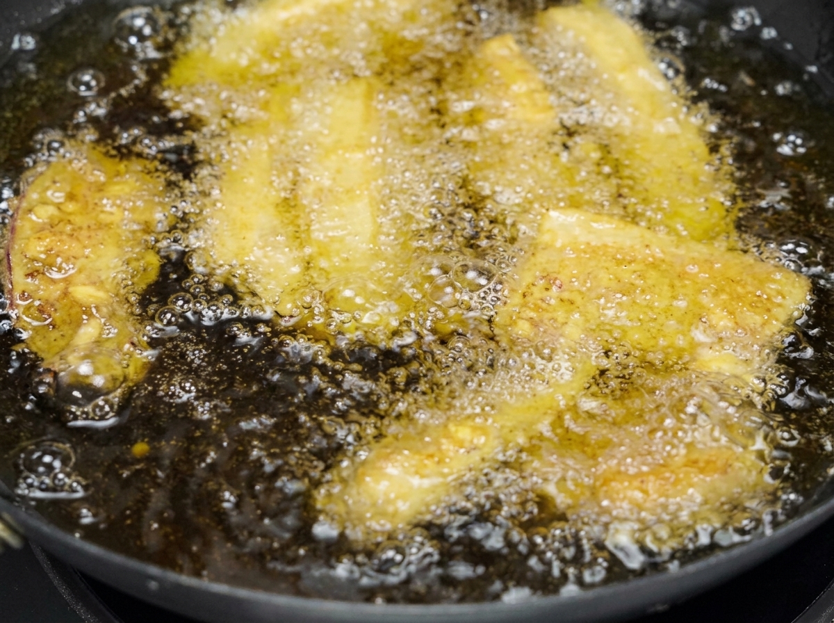 黄金色の泡が立つ揚げ鍋の中で、衣に包まれた何本もの豚バラ肉がゆっくりと揚がっている様子。
