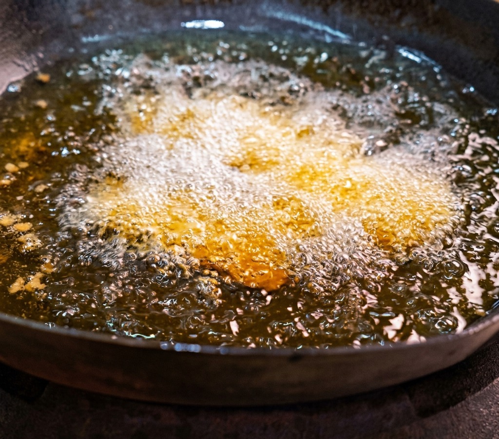 熱い油がパチパチと泡立つ中華鍋の中で、下味をつけた豚バラ肉のスライスが揚げられている様子。