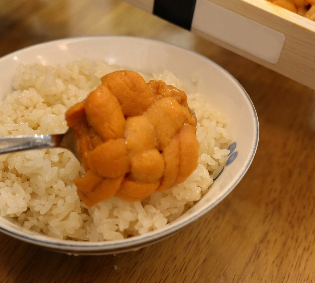 スプーンで崩れないようにすくい上げた、一粒一粒の形が美しいオレンジ色のウニを、すし飯の上に丁寧にのせている様子。