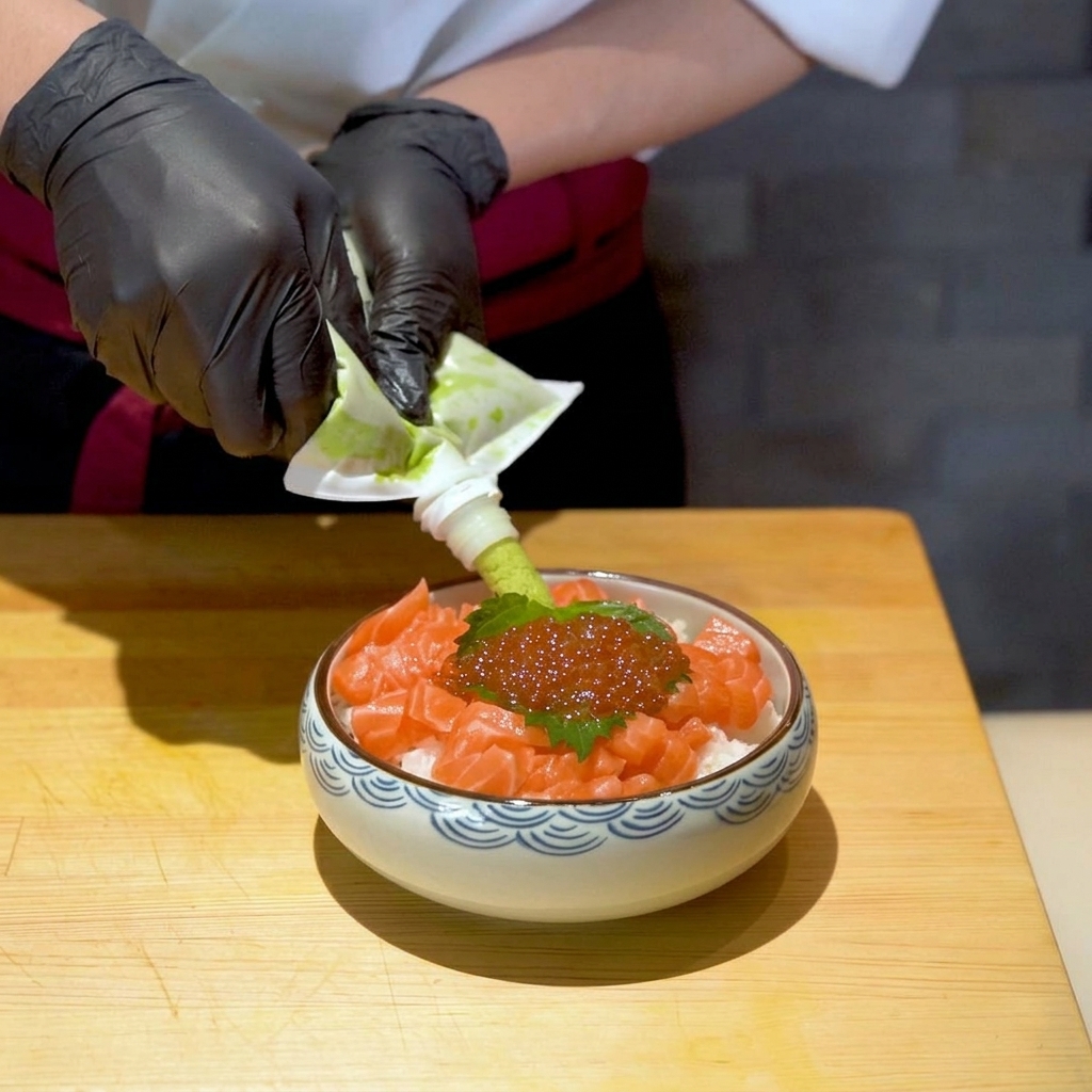 完成間近のサーモンといくらの親子丼の、大葉の脇にチューブから鮮やかな緑色の生わさびを少し絞り出している様子。