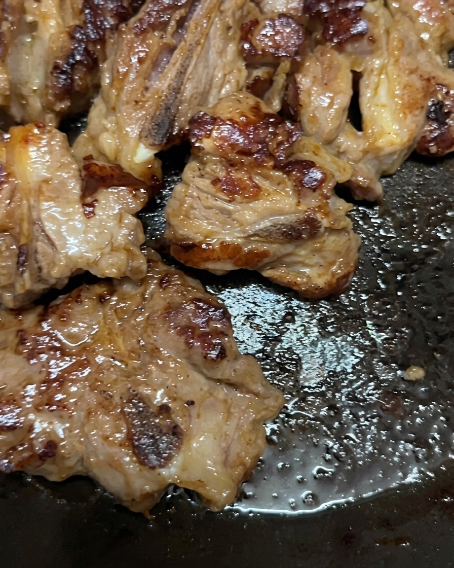 フライパンで香ばしく焼かれ、ひっくり返されて深みのあるキツネ色の焼き目がついた豚スペアリブ。