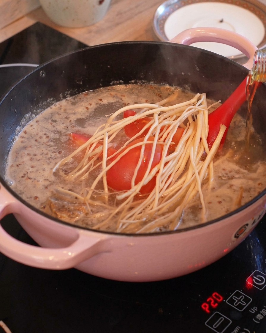 トマトや白い根菜が入った透明感のある沸騰スープに、ボトルから料理酒が回し入れられている様子。