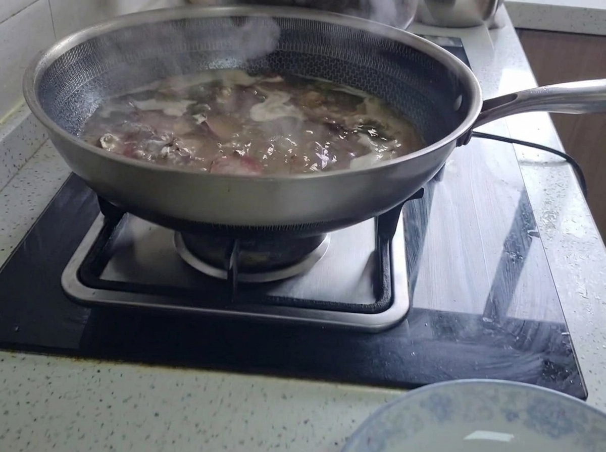 キッチンのコンロの上で、大きな中華鍋に張ったお湯で塩漬け豚スペアリブがコトコトと煮えている様子。