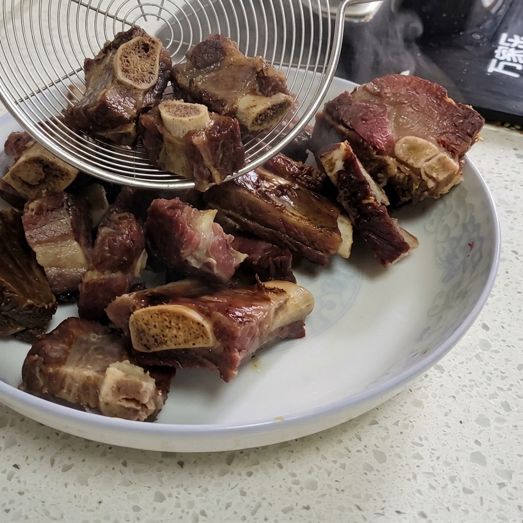 湯気が上がる中華鍋から、金属製の網じゃくしを使って茹で上がった塩漬け豚スペアリブをすくい上げ、お皿に移している様子。