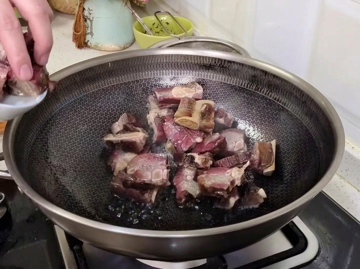 熱した中華鍋に、水気を切った塩漬け豚スペアリブを小さなお皿から丁寧に入れて炒め始めようとする手元。