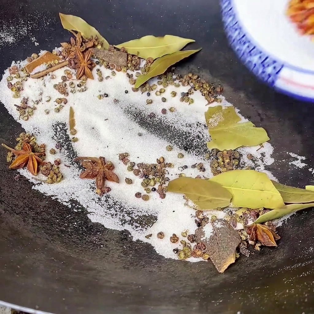 ほんのり色づいた塩やスパイスが入った中華鍋に、器から真っ赤な粉唐辛子を投入している様子。