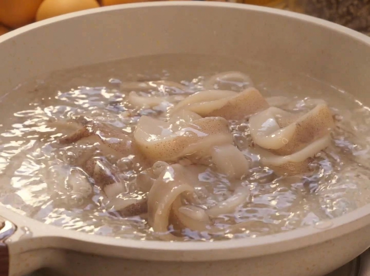 勢いよく沸騰したお湯の中で、新鮮な白いイカのリングが湯通しされている様子。