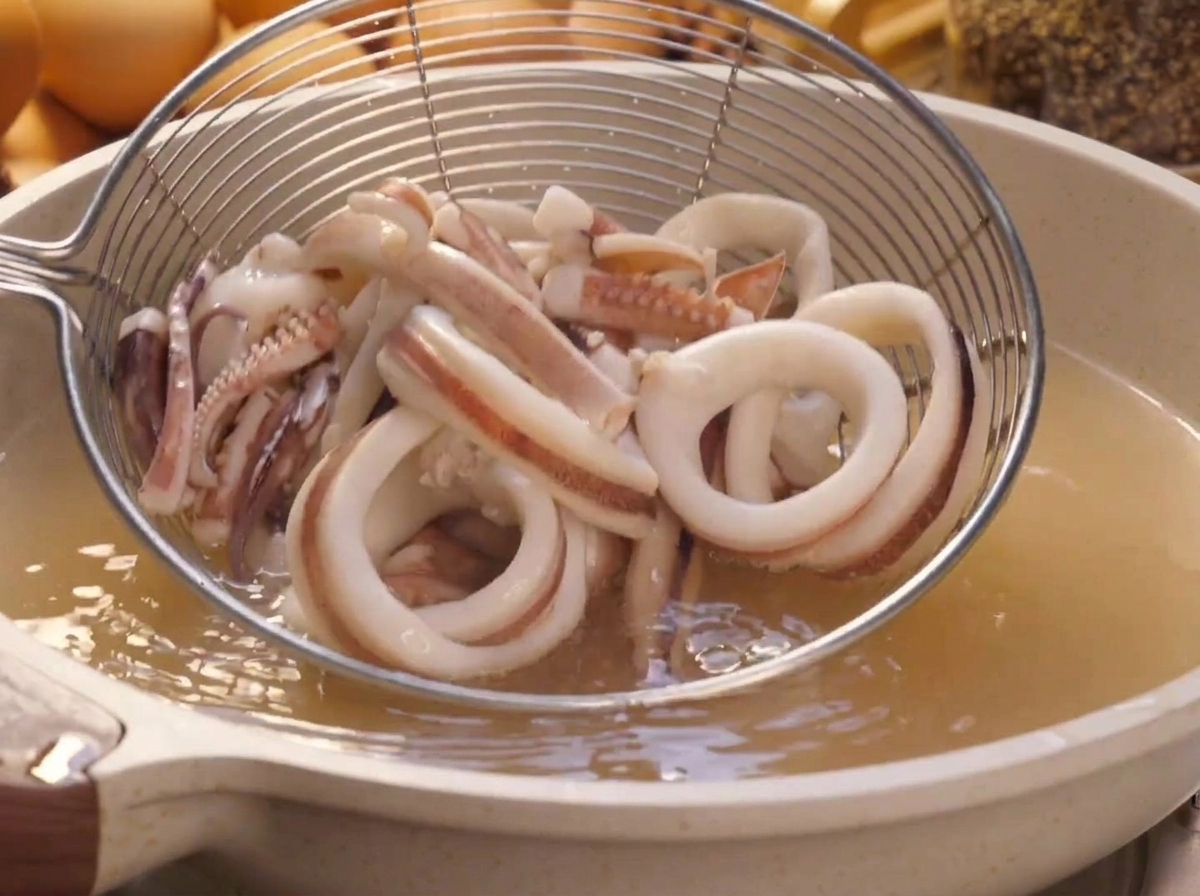 沸騰したお湯から、網じゃくしを使って湯通しした白いイカのリングをすくい上げている様子。