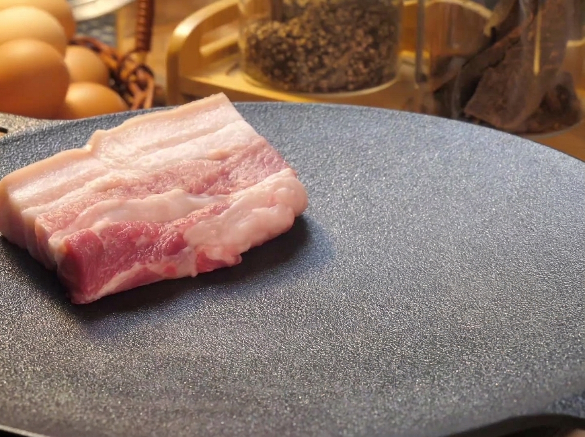 熱した黒い鉄板の上に、厚切りの生の豚バラ肉が並べられて焼かれている様子。